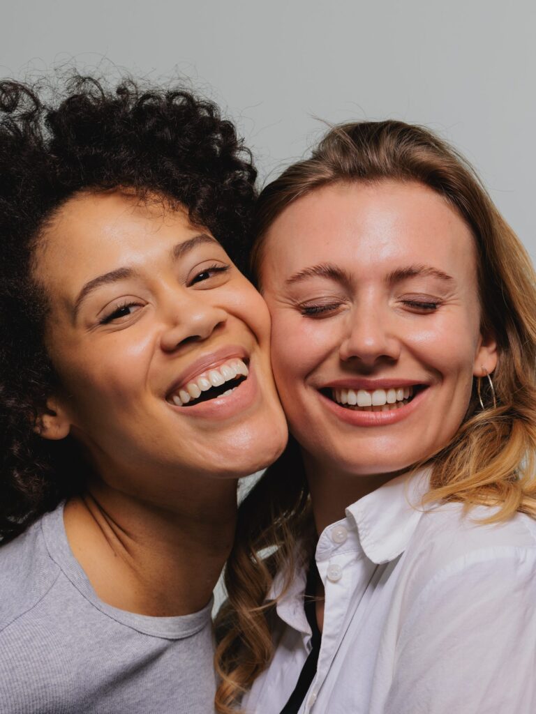 Zwei Frauen lachen Wange an Wange – gesunde, gepflegte Zähne