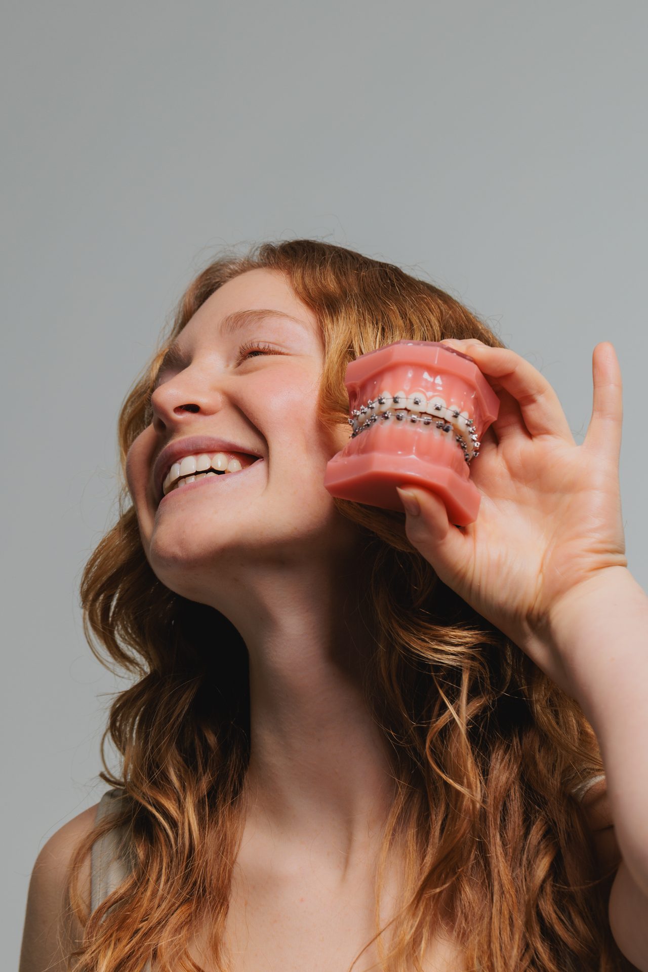 Jugendliche hält ein Zahnmodell mit Brackets neben ihr lachendes Gesicht